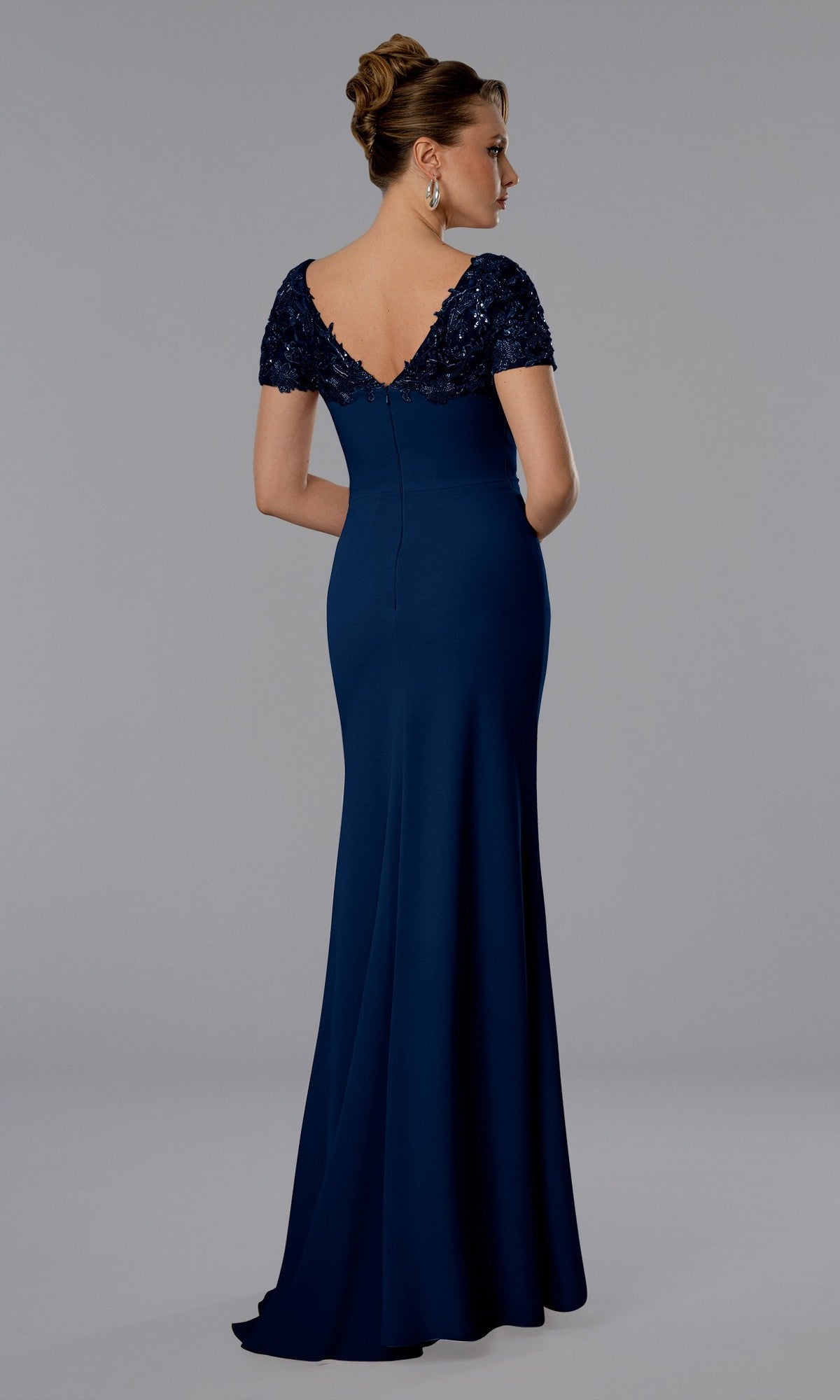 Woman wearing the Stella Couture 25368 navy long formal dress, featuring a fitted floor-length silhouette, beaded lace short sleeves, and a deep V-back, standing against a neutral background.